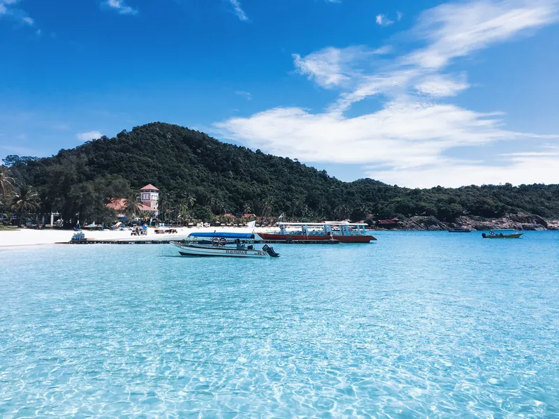 Beach with clear blue water, boats and a green island behind