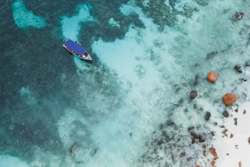 Drone view of one boat on turquoise water near a rocky shore