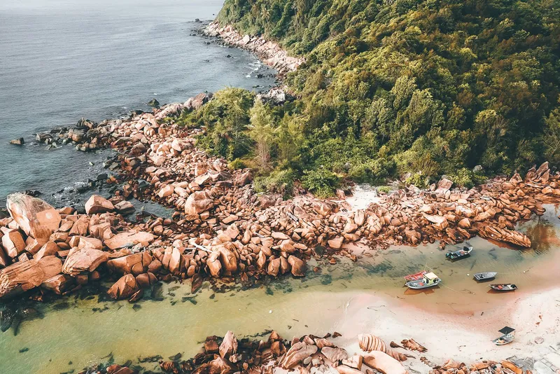Boats moored near a sandy beach and a stone breakwater, seen from above