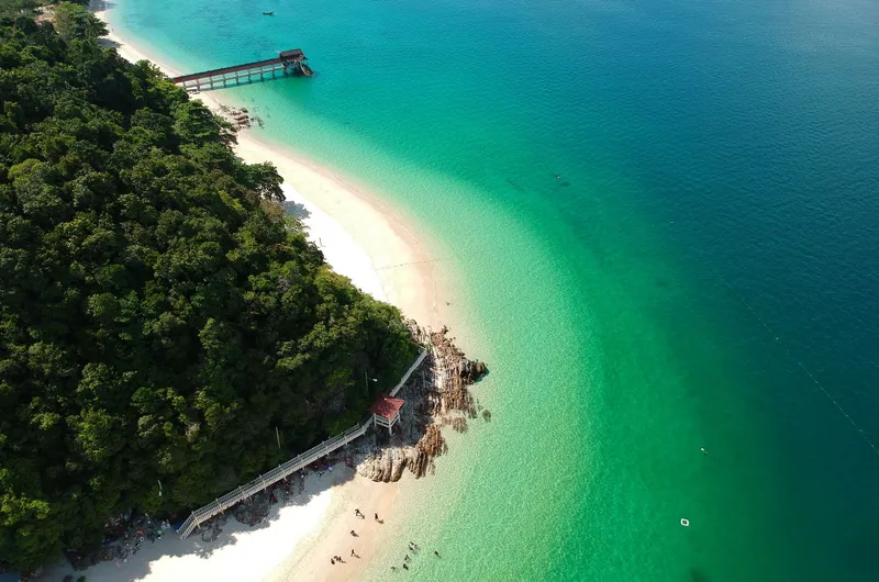 Aerial view of a beach with white sand, turquoise water and trees