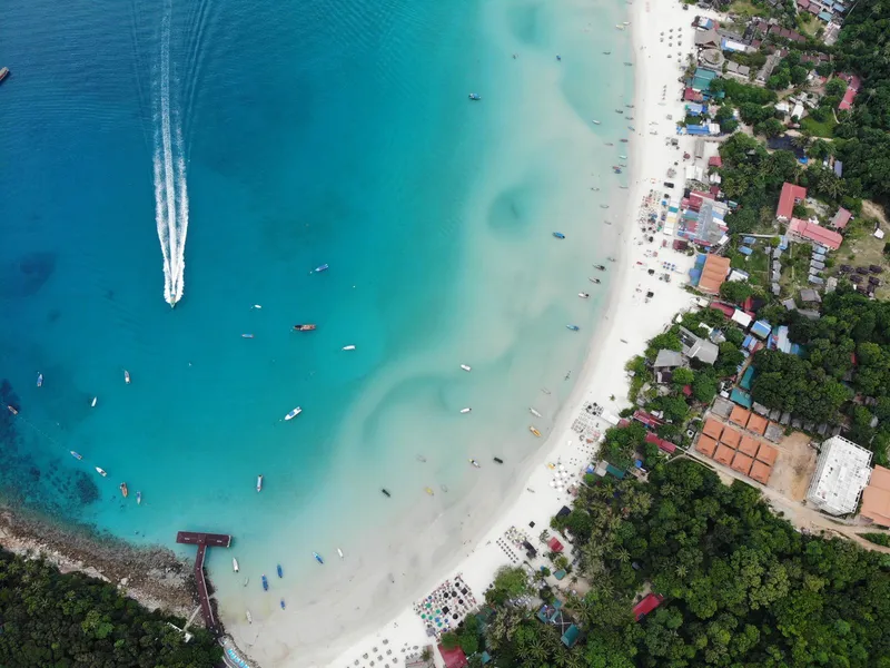 Drone view of a forested shore with houses and boats offshore